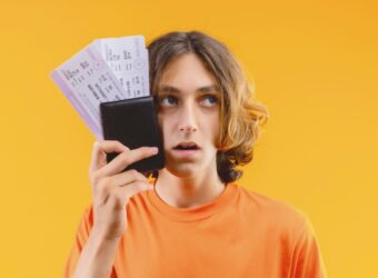 young-handsome-guy-orange-t-shirt-holding-air-tickets-looking-aside-confused-with-sad-expression (1)