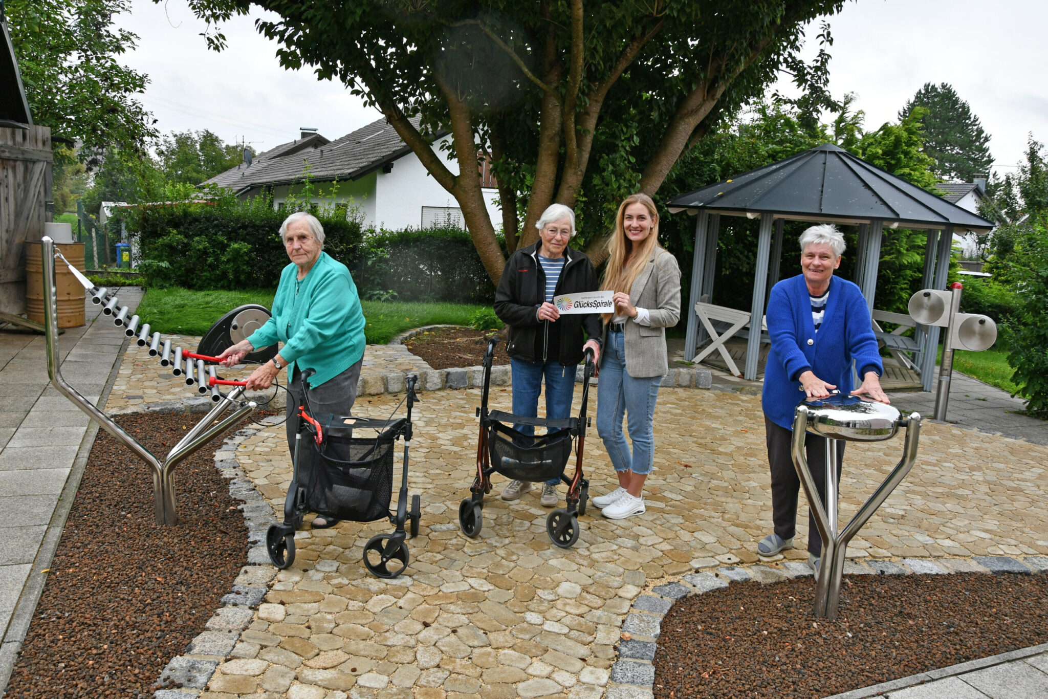 Foto: Im Caritas-Seniorenheim Ingolstadt-Gerolfing ist der Garten erneuert worden. Während Adelheid Neumaier (links) am Xylophon Harmony Glockenspiel und Edith Beringer (rechts) an der Babel Drum Spaß finden, zeigen sich Ursula Meyer und Einrichtungsleiterin Sarah Jacoby (Zweite von rechts) für die Unterstützung der GlücksSpirale dankbar. Foto: Caritas / Peter Esser
