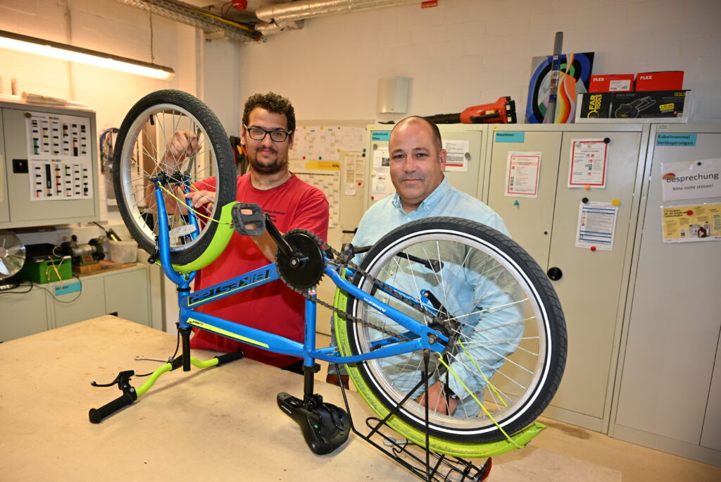 Daniel Alter (links), der eine geistige Beeinträchtigung hat, macht ein Check-up an einem Fahrrad eines Schülers im Caritas-Zentrum St. Vinzenz. Sein Vorgesetzter Dominic Walter ist mit seiner Arbeit zufrieden. Foto: Caritas / Peter Esser
