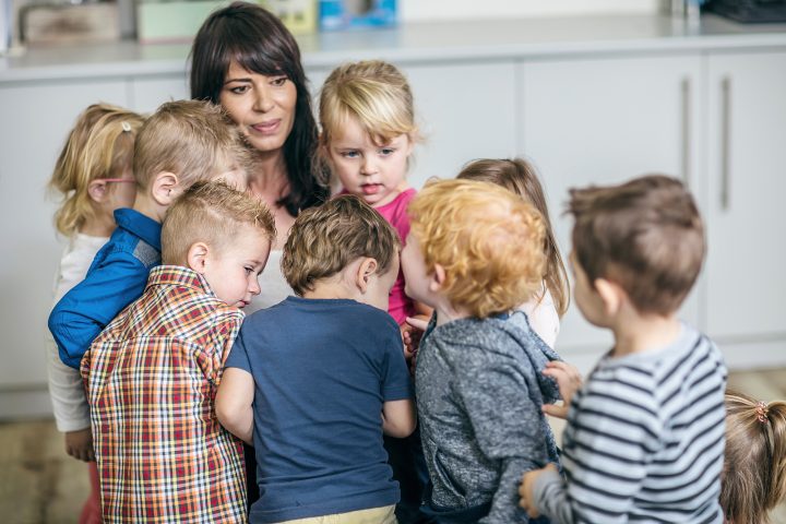 Kleinkinder stehen um ihre Erzieherin herum.