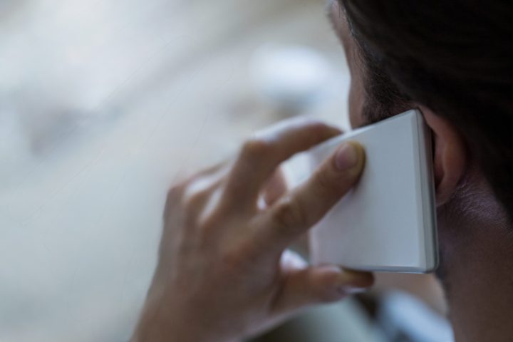 Rear view of man talking on the mobile phone and using laptop in coffee shop