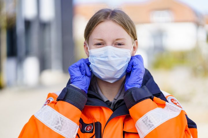 Eine Helferin steht  am Mittwoch (15.04.20) für ein Symbolfoto mit Mundschutz und Handschuhen an einem Fahrzeug des Johanniter-Hausnotrufs in Wunstorf (Region Hannover).
Foto: Johanniter/Stefan Simonsen