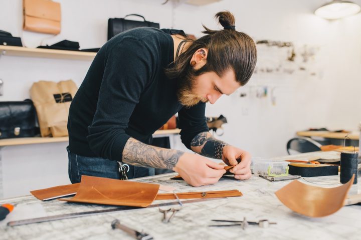 Working process of the leather bag in the leather workshop. Man holding crafting tool and working. Work table background.