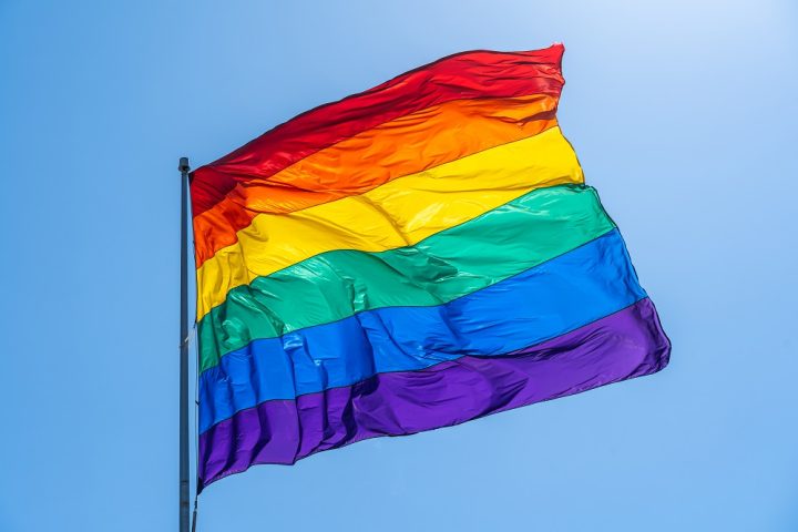 Rainbow gay pride flag on a blue sky.