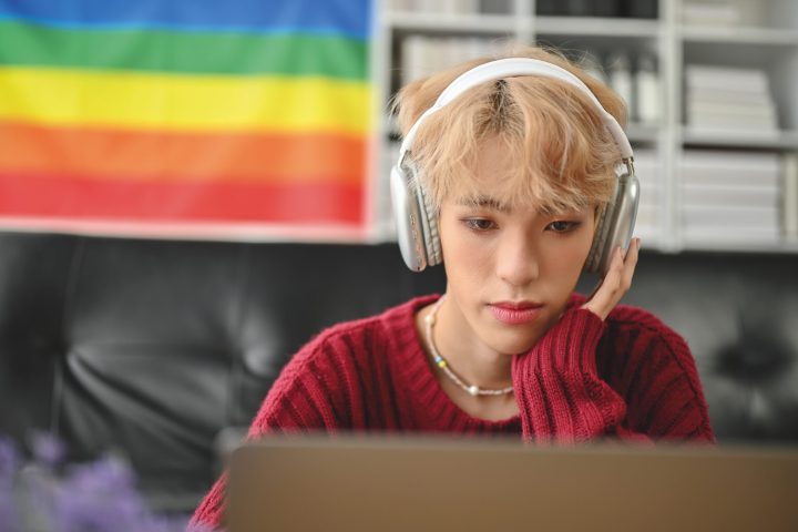 An attractive young Asian gay man focuses on his work on laptop or reads something on a website, looking at his laptop screen, using his laptop computer in the living room.
